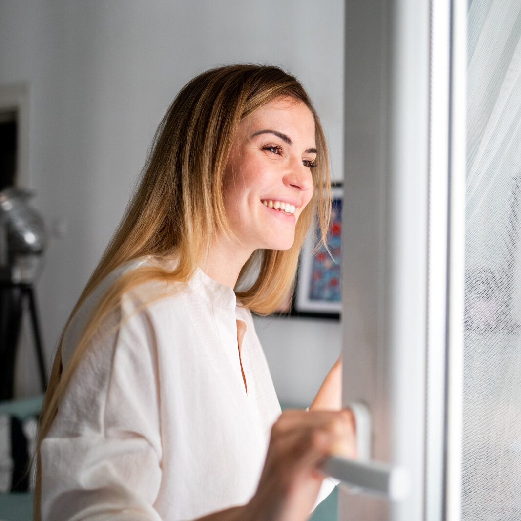 Frau öffnet Fenster und atmet frische Luft ein Frau öffnet Fenster und atmet frische Luft ein