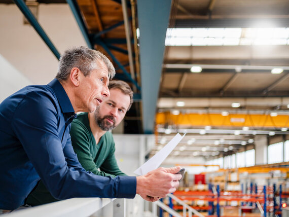 Two men standing in a hall, engaged in a discussion about plans for energy-efficient cooling solutions