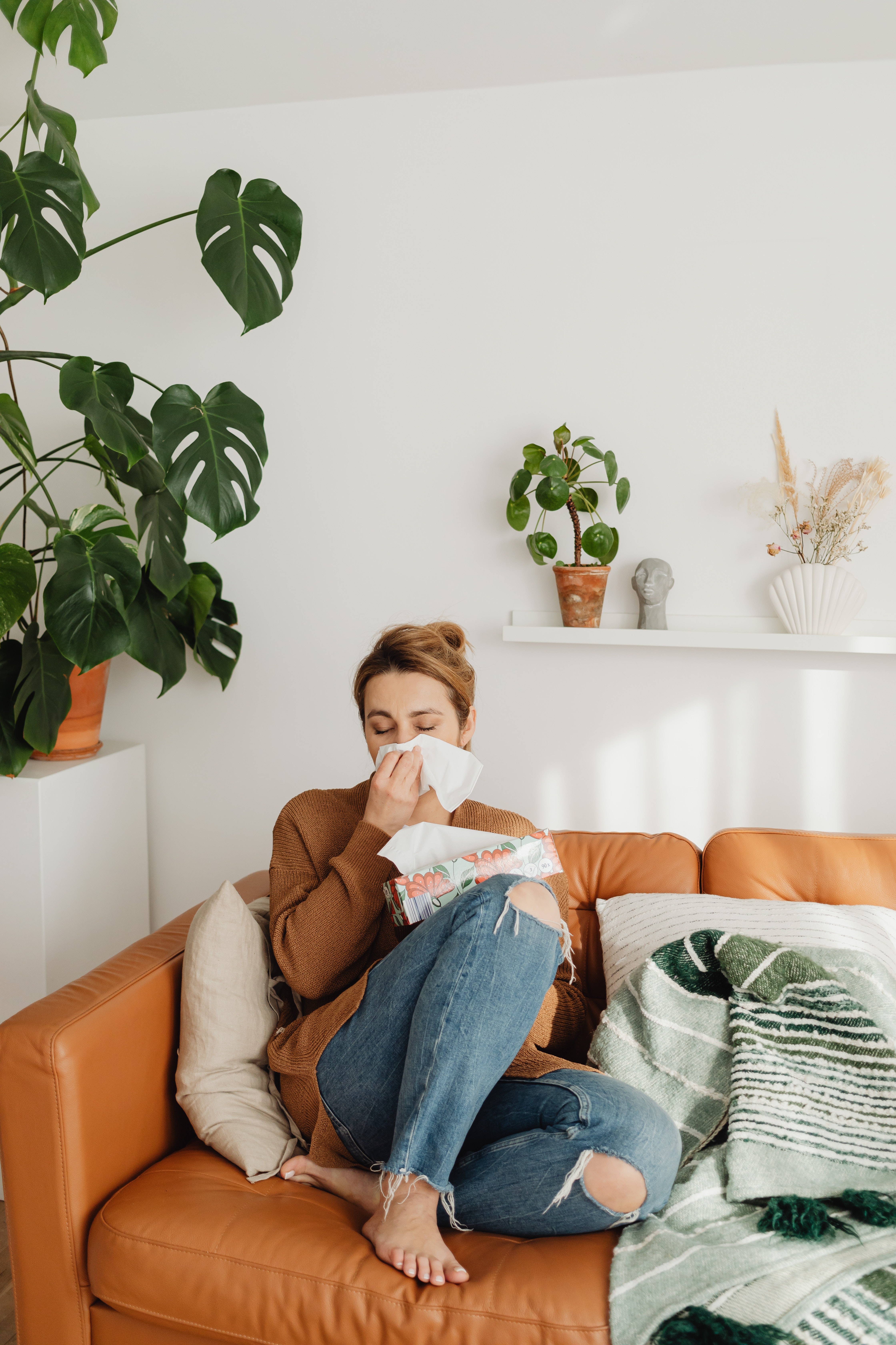 Woman with allergy symptoms sitting on her coutch at home and cleaning her nose